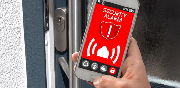 Alarmanlage per App steuern – volle Kontrolle über Ihr Zuhause. Smartphone mit geöffneter Sicherheits-App vor Hauseingangstür, Symbol für moderne Alarmanlagensteuerung per App.